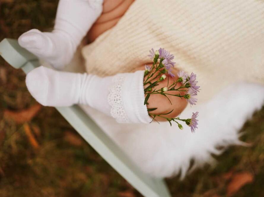 A baby wearing white socks and flowers on a rocking chair.