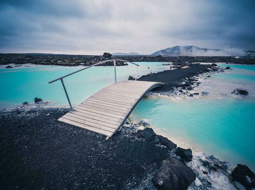 A wooden bridge over a blue lagoon in iceland.