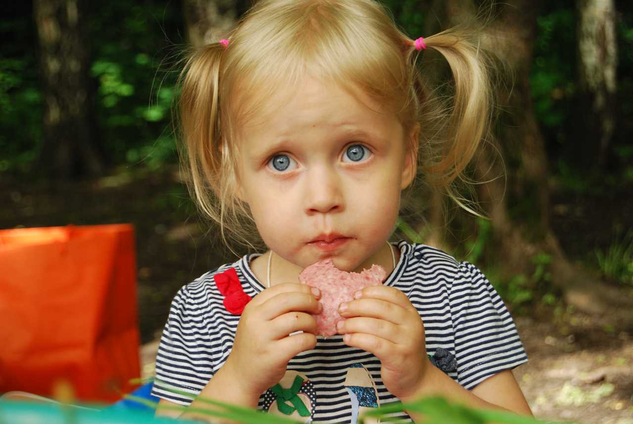 A little girl eating a sandwich in the woods.