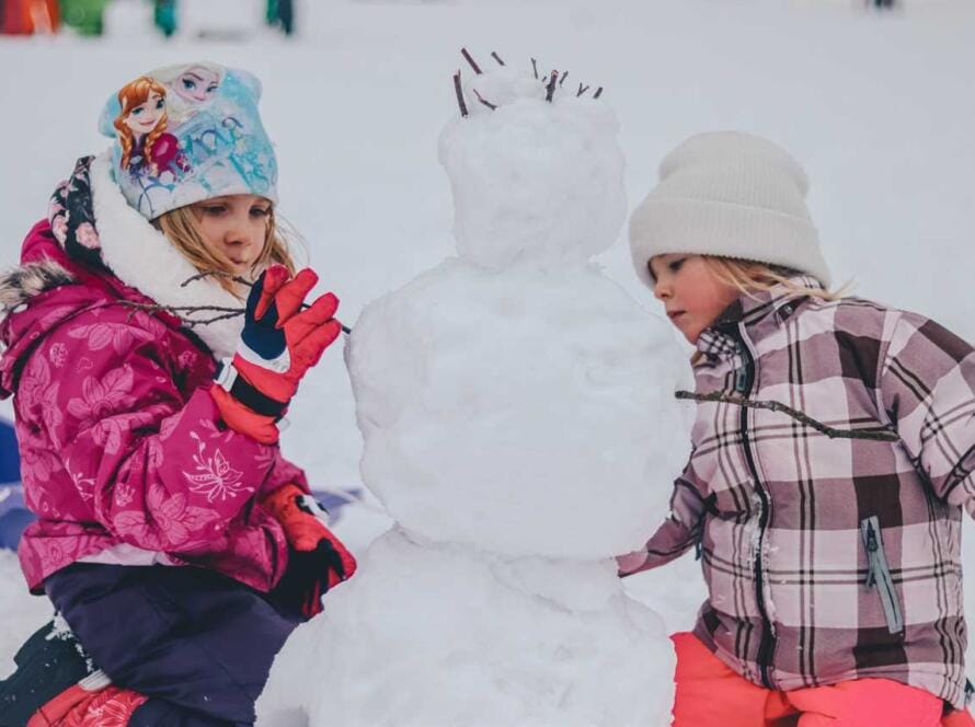 Two girls playing with a snowman in the snow.