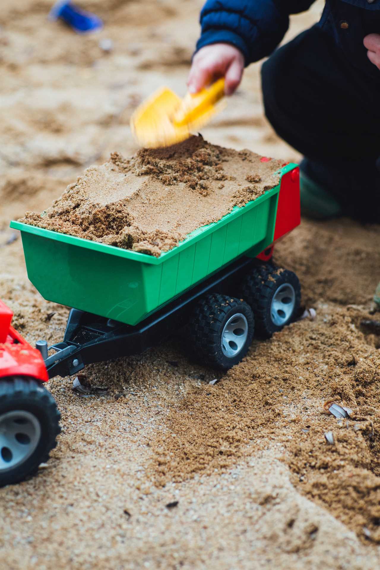 A boy playing with a toy truck on the sand.