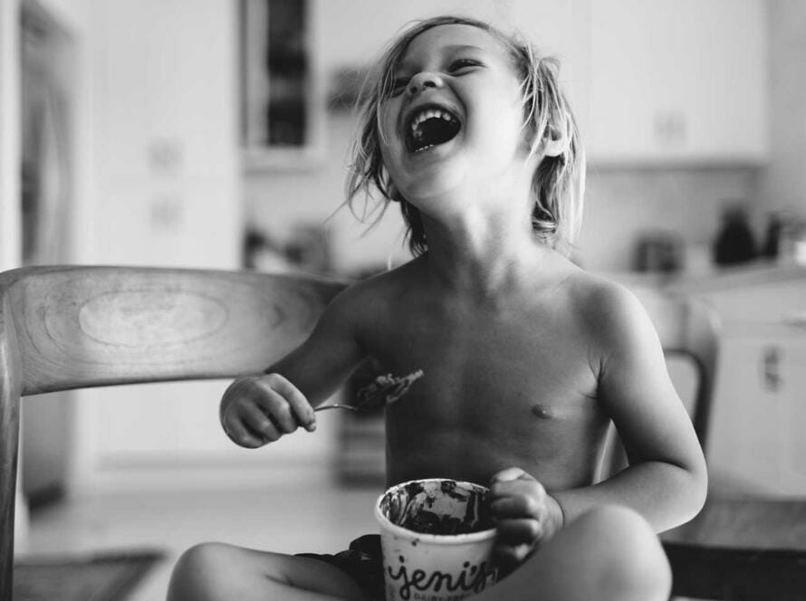 A young boy sitting on a chair and eating a bowl of ice cream.