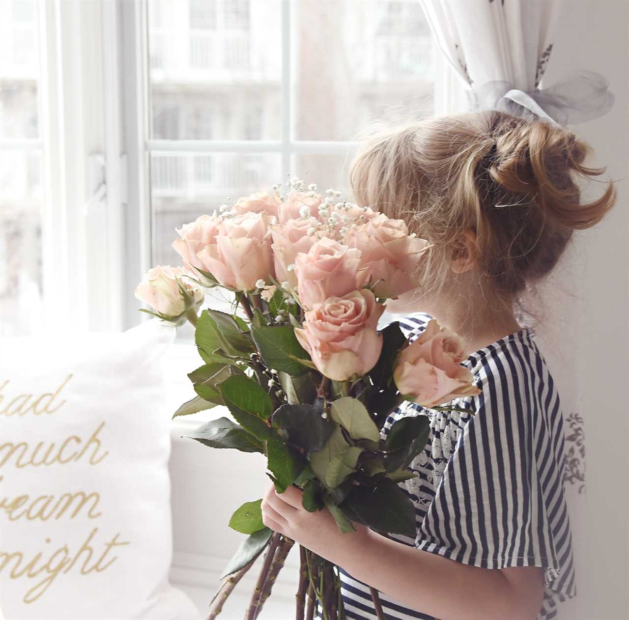 A little girl holding a bouquet of roses in front of a window.