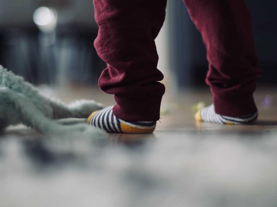 A child's feet on the floor with a stuffed animal.