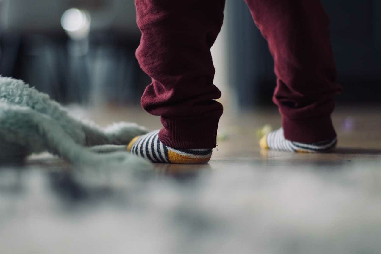 A child's feet on the floor with a stuffed animal.