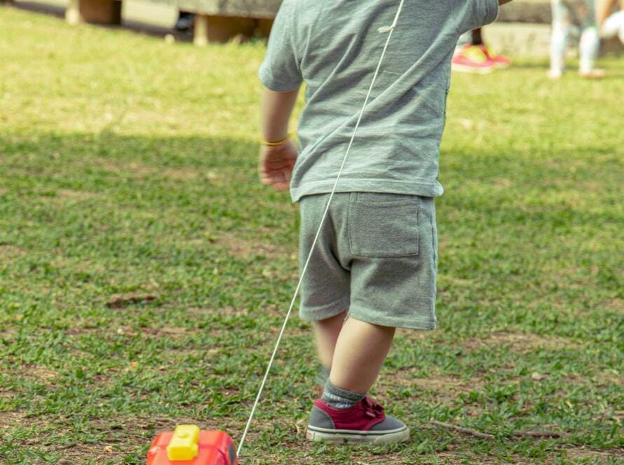 A young boy is pulling a toy train on a grassy field.