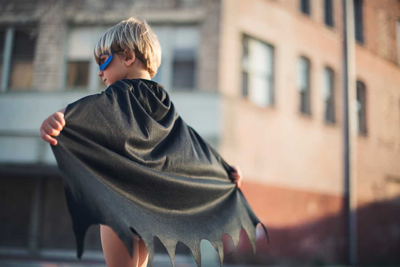 A young boy dressed as a batman in a city.