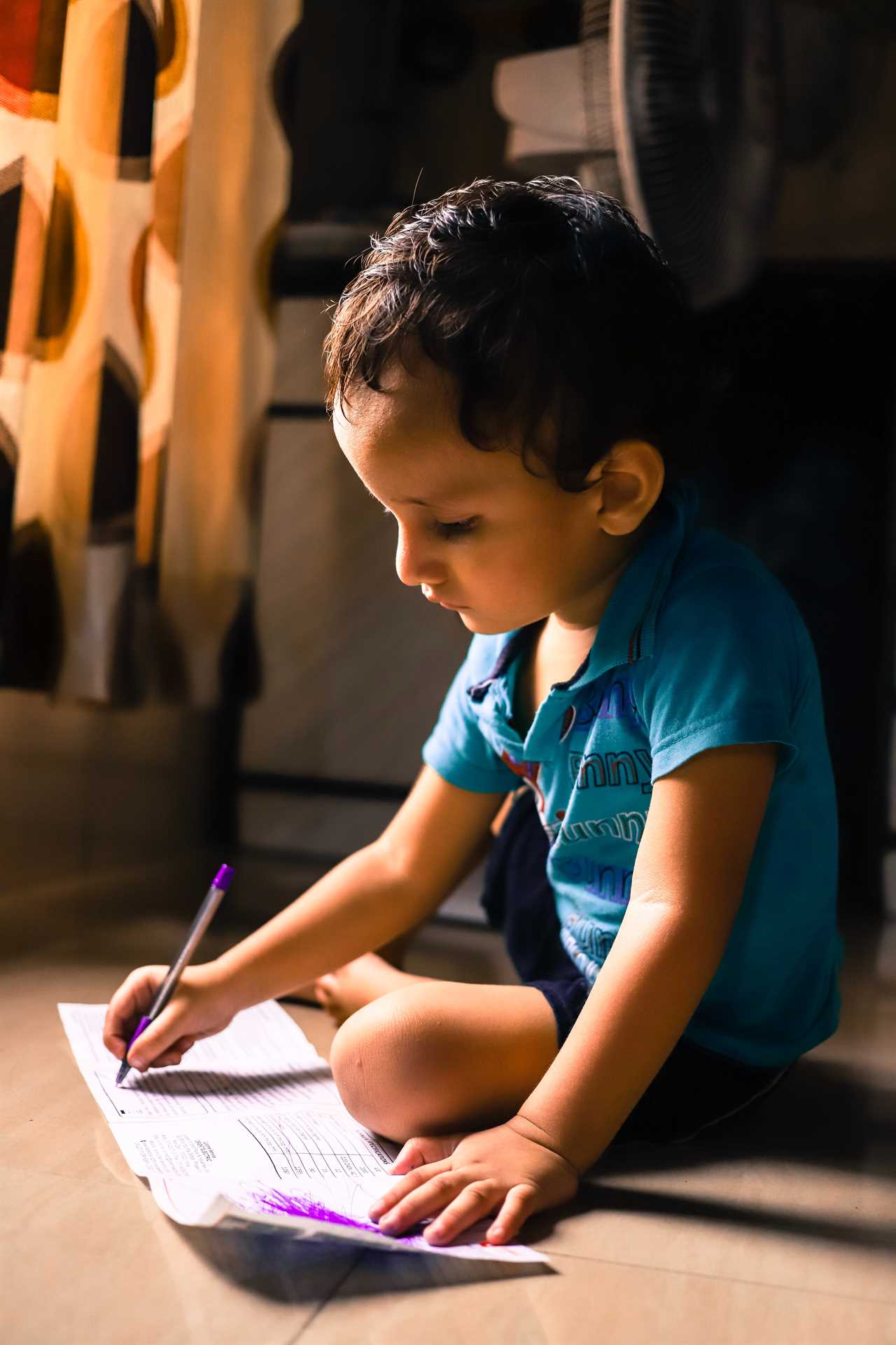 A young boy sitting on the floor with a pen and paper.