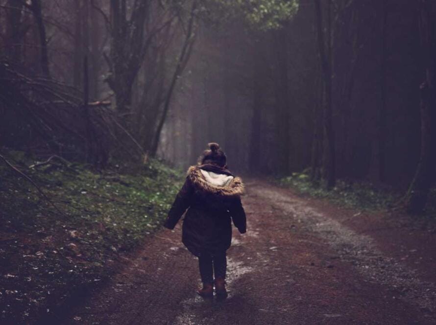 A woman walking down a path in the woods.