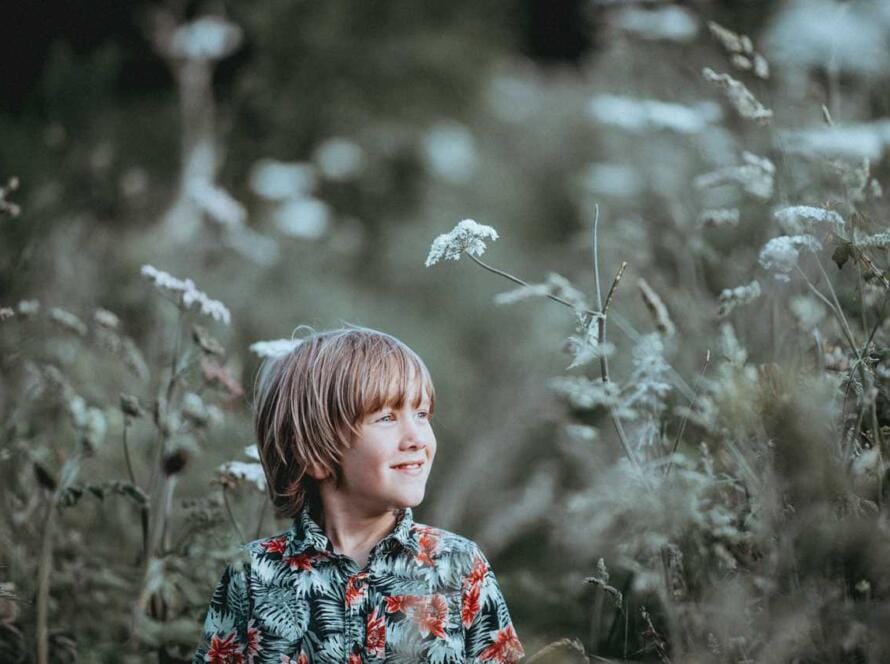 A young boy is standing in a field of tall grasses.