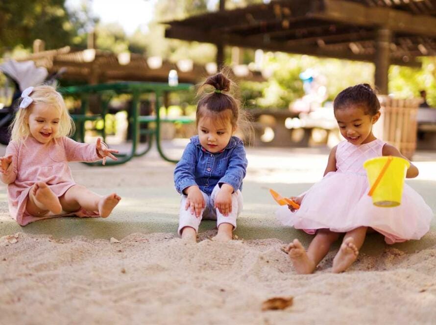 Three little girls playing in the sand at a park.