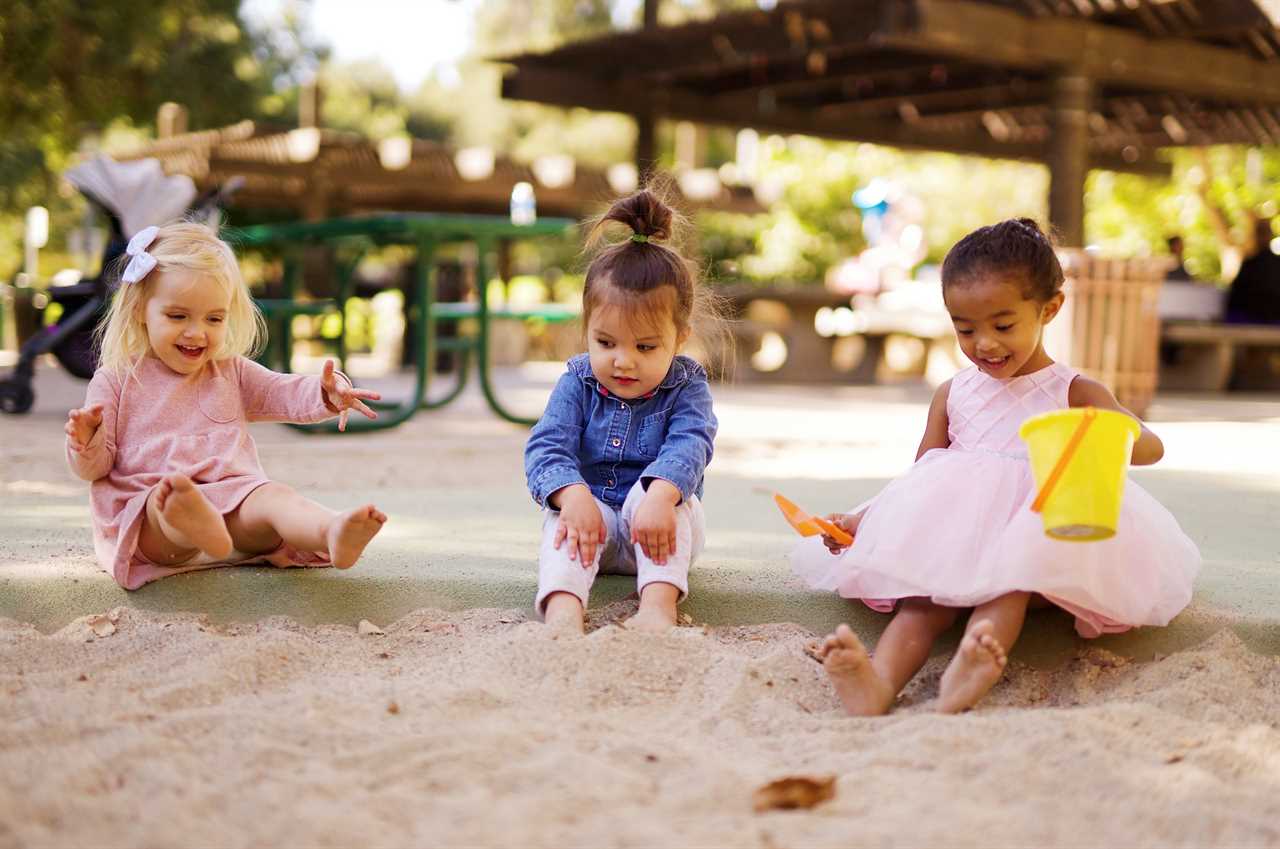 Three little girls playing in the sand at a park.