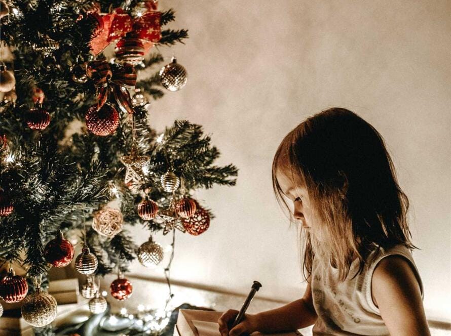 A girl is reading a book in front of a christmas tree.