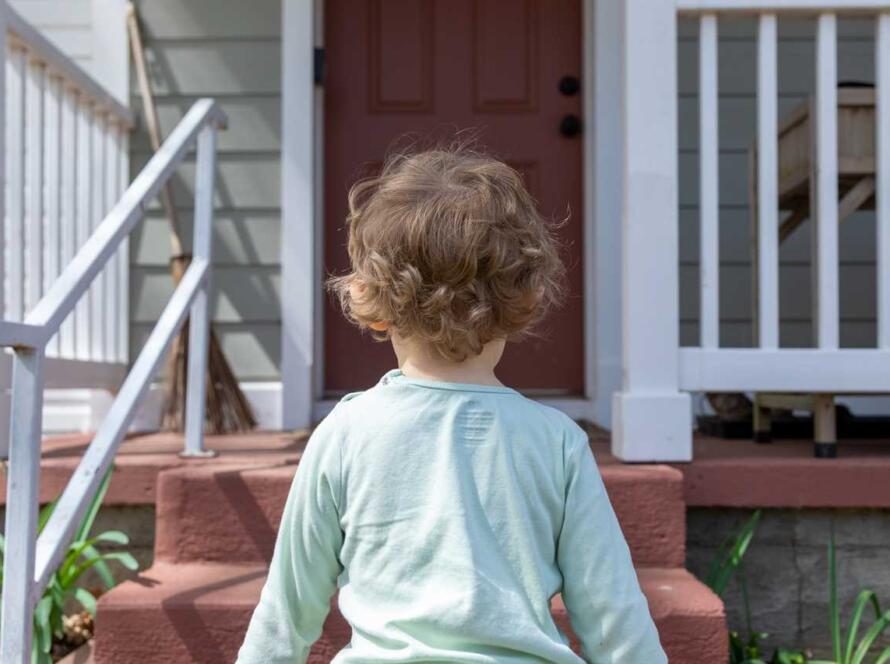 A young boy standing on the steps of a house.