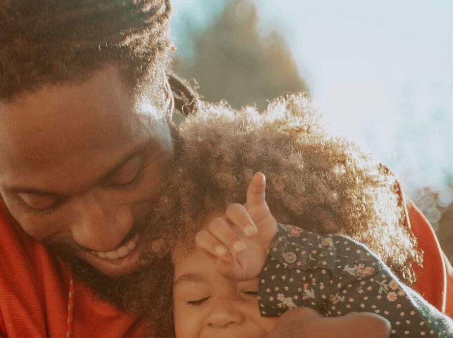 A man hugging a little girl with dreadlocks.