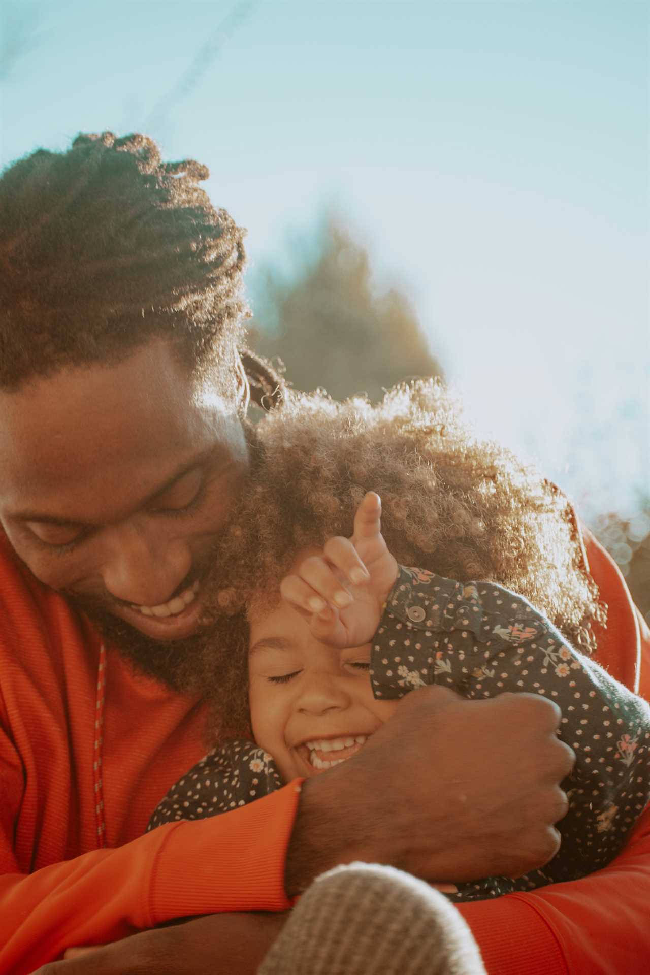 A man hugging a little girl with dreadlocks.