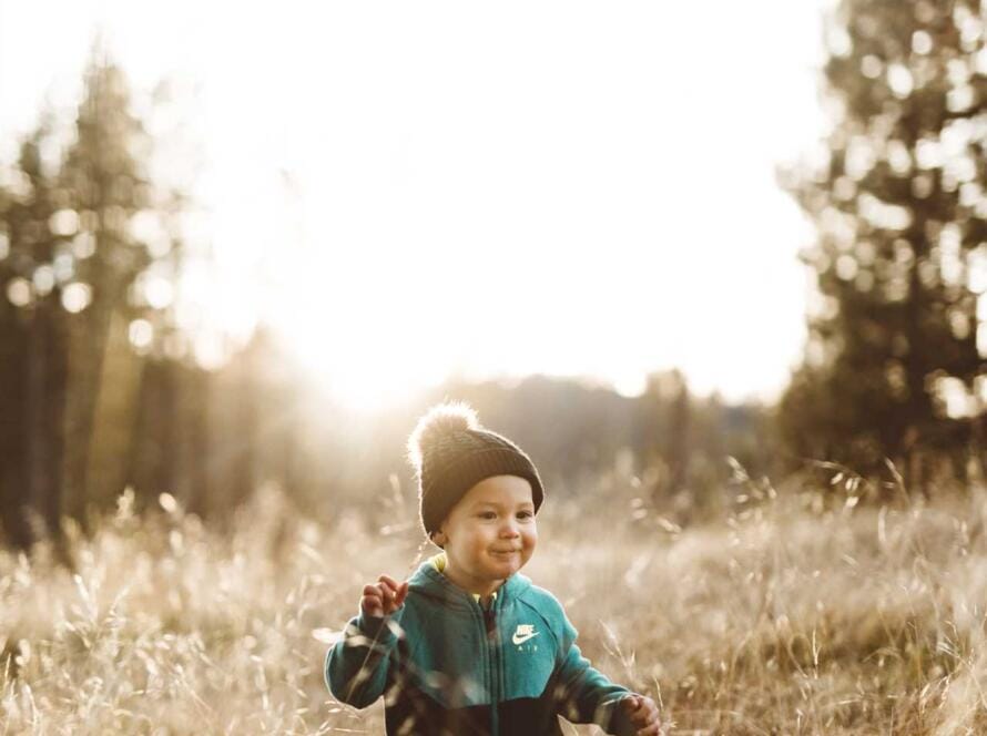 A baby boy running through tall grass in a field.