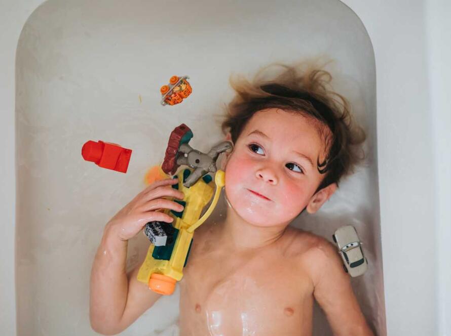 A young boy laying in a bathtub with toys.