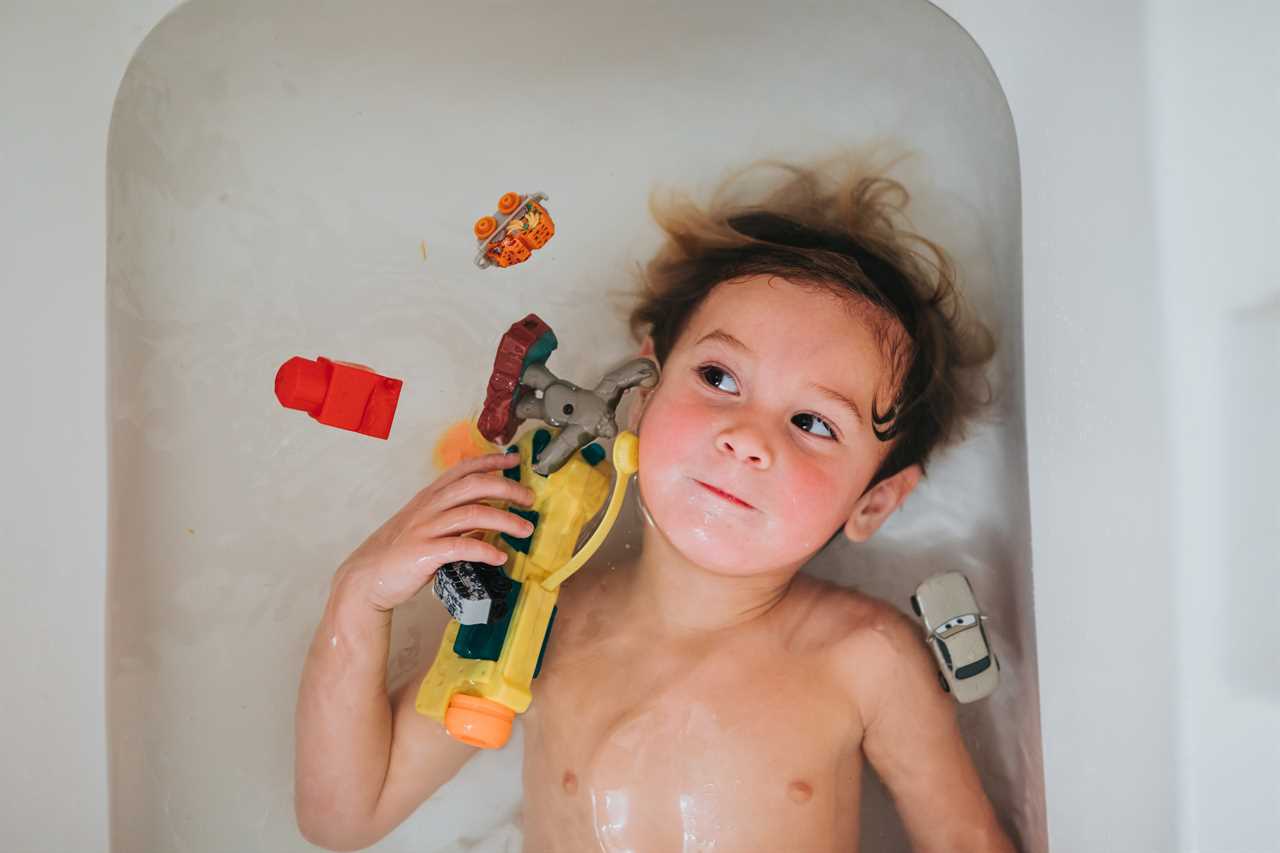 A young boy laying in a bathtub with toys.