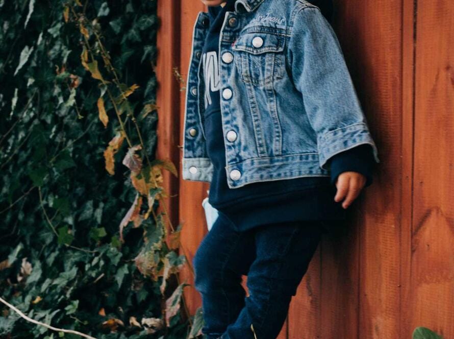 A little girl in a denim jacket leaning against a wooden fence.