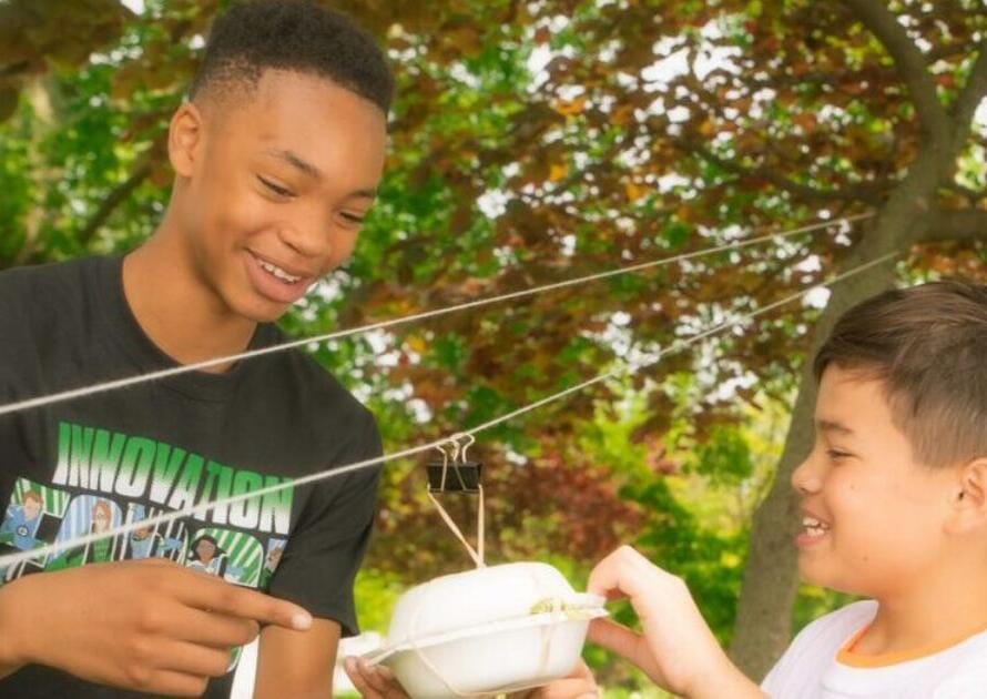 Two boys are holding a bowl of food in their hands.