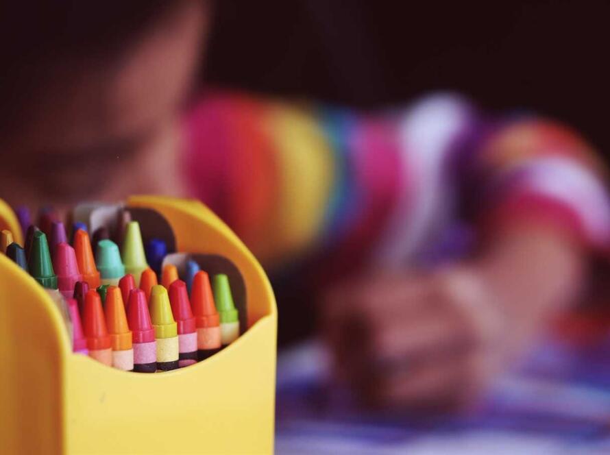 A child is drawing with crayons in a yellow holder.