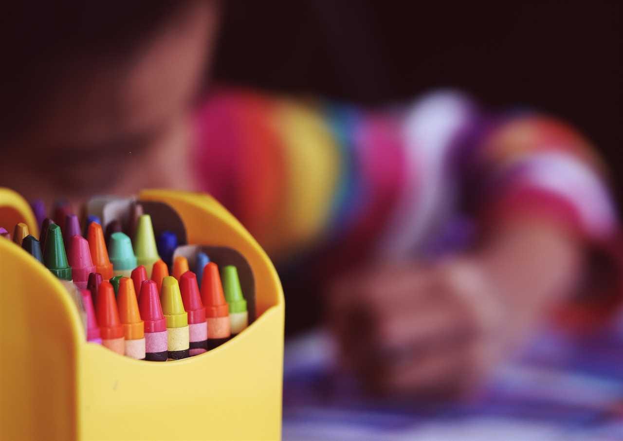 A child is drawing with crayons in a yellow holder.