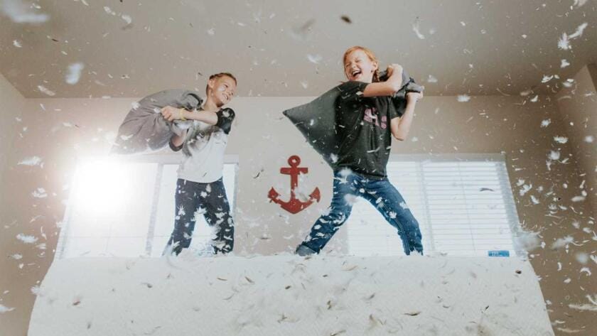 Two boys playing on top of a mattress in a bedroom.