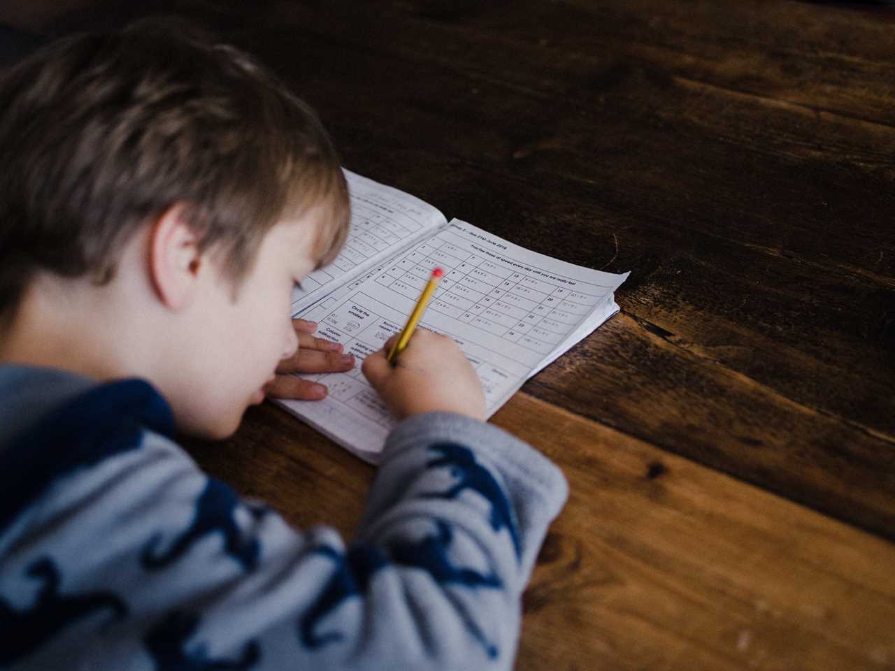 A young boy writing in a notebook on a wooden table.