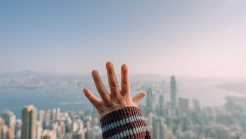 A woman's hand reaching out to the skyline of hong kong.