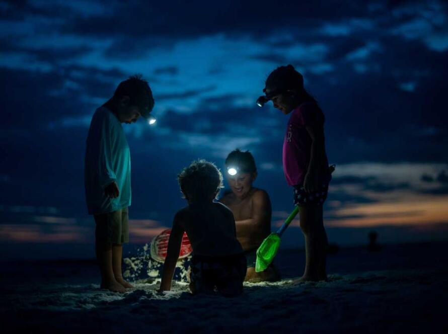 A group of people playing in the sand at night.