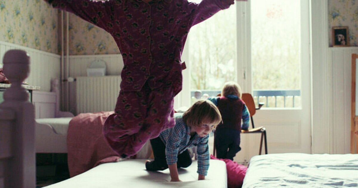 A girl in a pink pajama jumps on top of a bed.