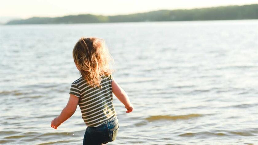 A little girl running in the water near a lake.