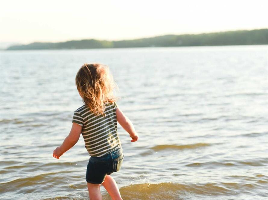 A little girl running in the water near a lake.