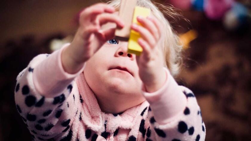 A little girl in a pink pajama holding a toy.