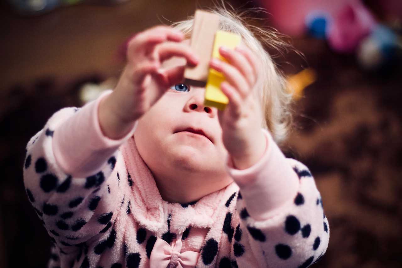 A little girl in a pink pajama holding a toy.