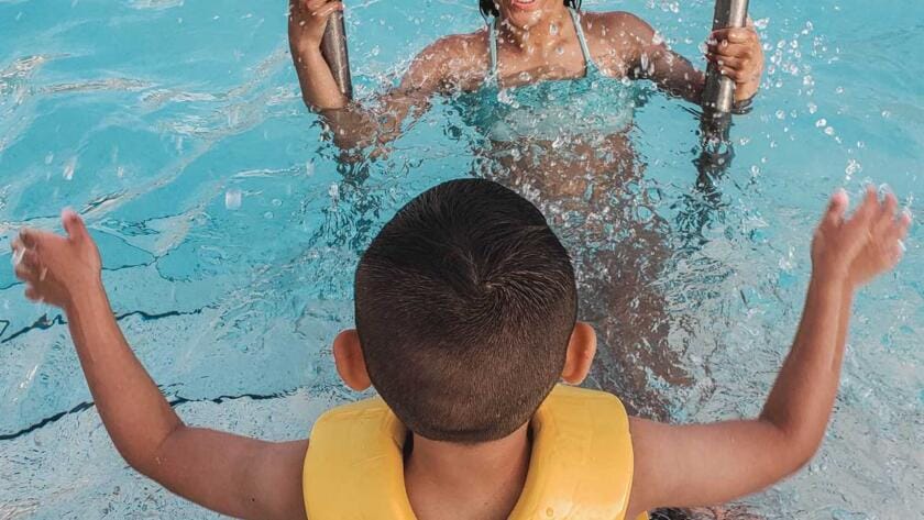 A woman and child in a life jacket in a swimming pool.