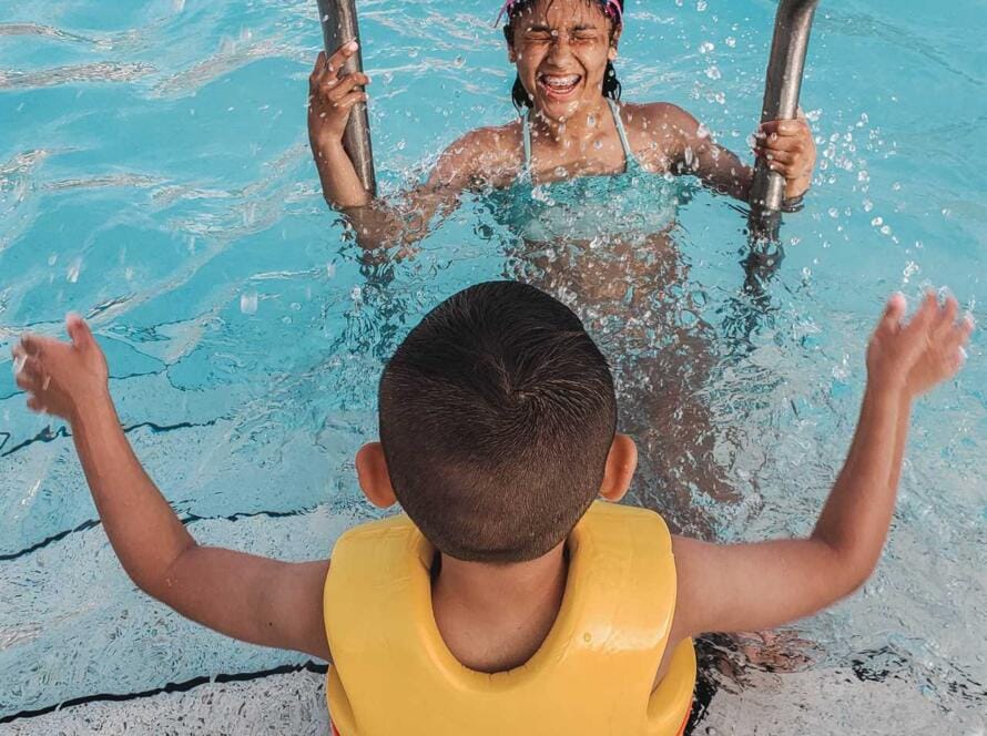 A woman and child in a life jacket in a swimming pool.