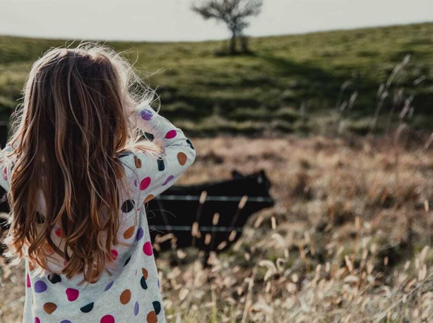 A girl looking at a cow in a field.