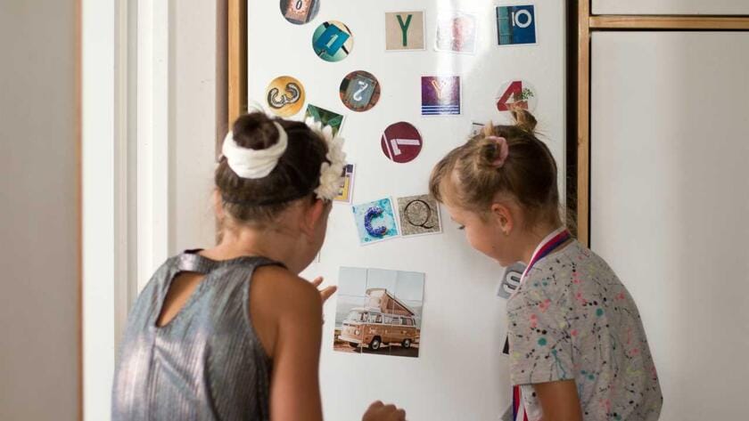 Two girls sitting on the floor in front of a refrigerator.