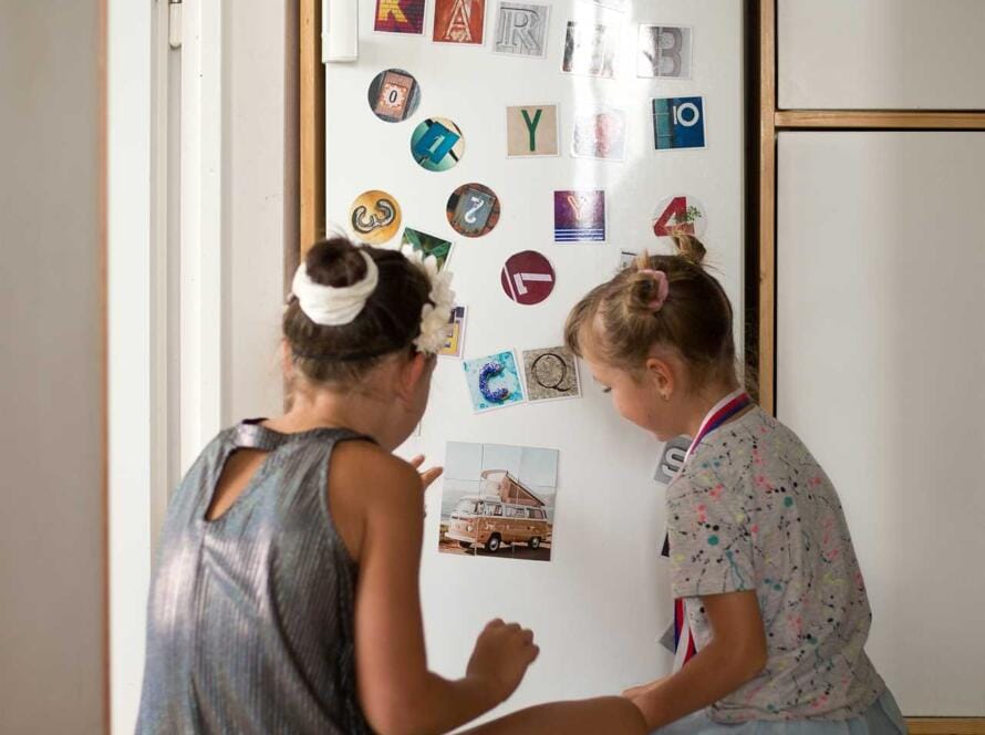 Two girls sitting on the floor in front of a refrigerator.