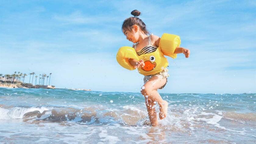 A little girl running in the ocean wearing a yellow life jacket.