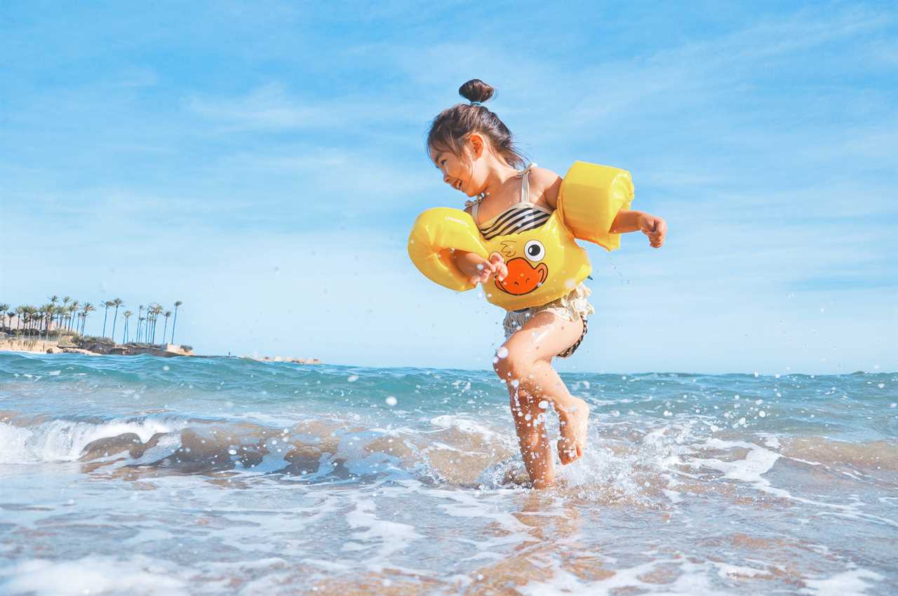 A little girl running in the ocean wearing a yellow life jacket.