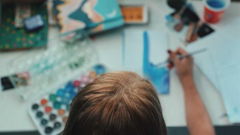 A child is sitting at a table with paints and brushes.