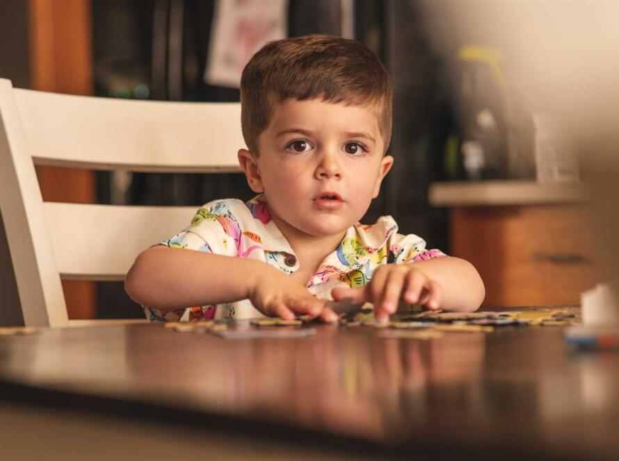 A young boy sitting at a table playing with puzzles.