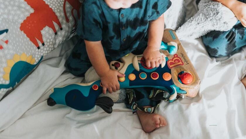 Two toddlers playing with a toy on a bed.