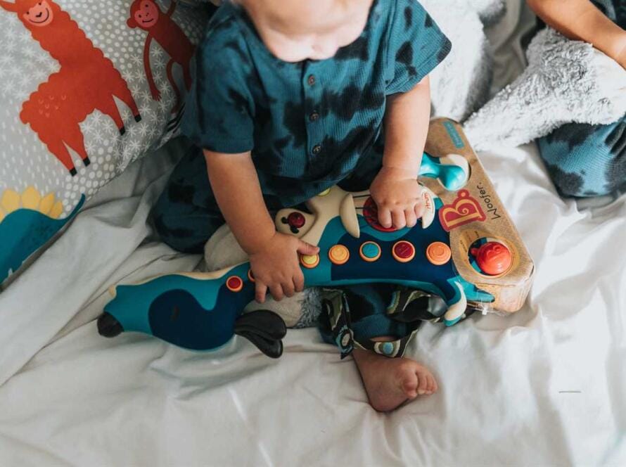 Two toddlers playing with a toy on a bed.