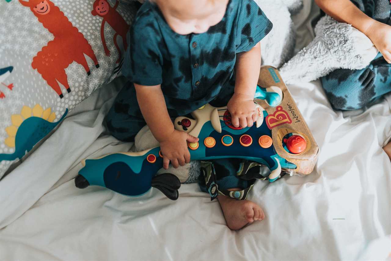 Two toddlers playing with a toy on a bed.