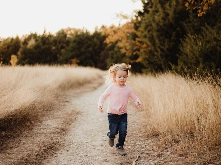 A little girl running down a dirt road at sunset.