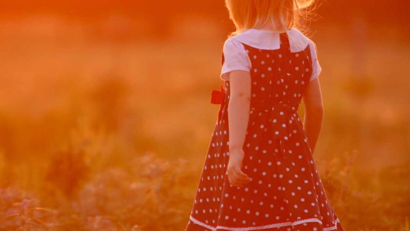 A little girl in a polka dot dress walking in a field at sunset.